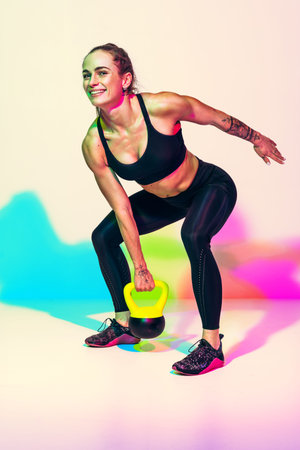 Sporty woman ready to swing the kettlebell up. Photo of woman in black sportswear on white...