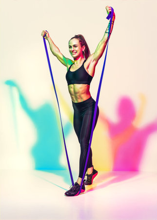 Strong woman working with resistance band. Photo of woman in black sportswear on white background...