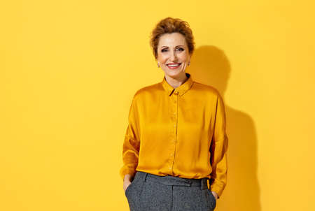Positive woman laughs happily. Photo of kind attractive woman in yellow shirt on yellow backgroundの写真素材