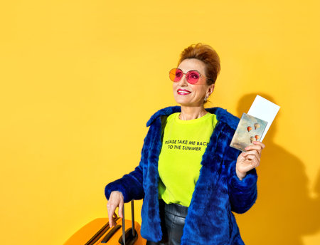 Happy woman is ready to travel. Photo of elderly woman wears pink glasses, dressed in fashionable...