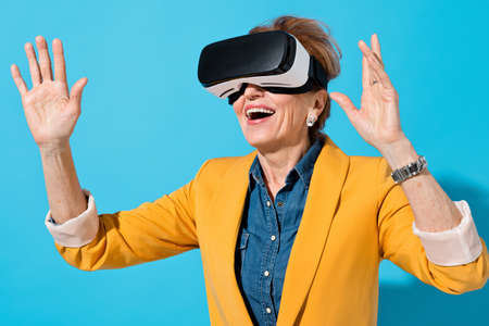 Mature woman with modern VR goggles. Photo of business woman in yellow blazer on blue backgroundの写真素材