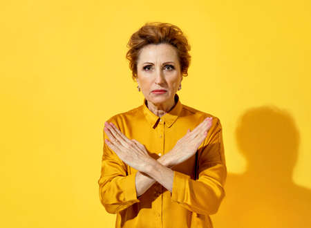 Woman crossed her arms in "no" or "stop" gesture. Photo of serious woman in yellow shirt on yellow backgroundの写真素材
