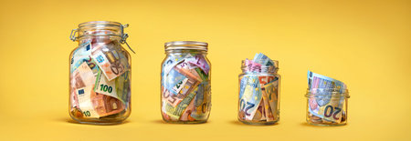 Four glass jars with savings, cash money (euro banknotes) banknotes) on yellow background