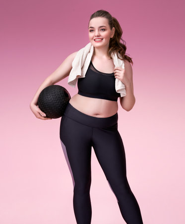 Sporty girl resting after training. Photo of pretty model with curvy figure in black sportswear on pink background. Sports motivation and healthy lifestyleの写真素材