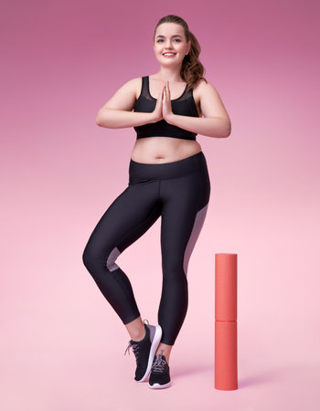 Young girl ready to yoga. Photo of pretty model with curvy figure in black sportswear on pink background. Sports motivation and healthy lifestyleの写真素材