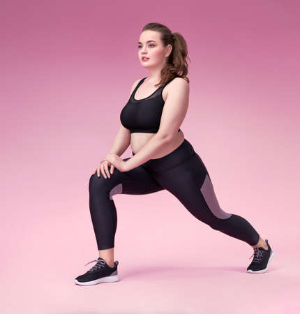 Warming up before training. Photo of pretty model with curvy figure in black sportswear on pink background. Sports motivation and healthy lifestyleの写真素材