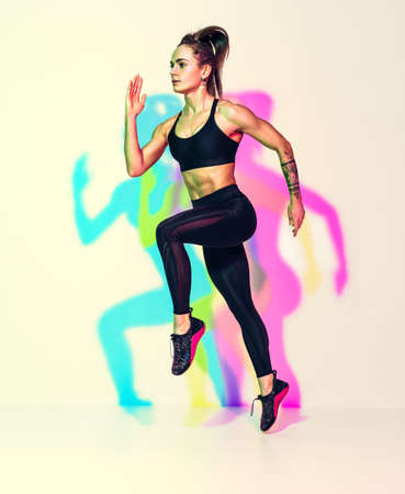 Sporty woman runner in silhouette. Photo of muscular woman in black sportswear on white background with effect of rgb colors shadows. dynamic movement. side view. Sport and healthy lifestyleの写真素材