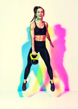 Strong woman jumping with kettlebell. Photo of sporty woman in black sportswear on white background with effect of rgb colors shadows. strength and motivation. full lengthの写真素材
