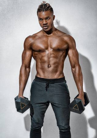 Sporty man resting after exercise with dumbbells on gray background. Photo of muscular man with...