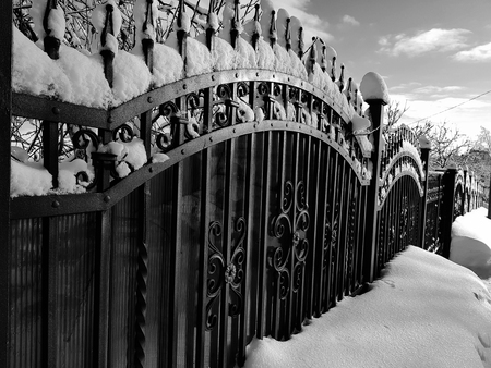 metal fence with forged elements near the house in icicles on the background of snow and the house in winterの写真素材