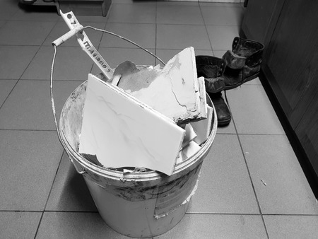 Repair construction and debris in a bucket with pieces of tile and plasterboard on the tiled floorの写真素材