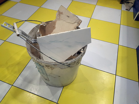Repair construction and debris in a bucket with pieces of tile and plasterboard on the tiled floorの写真素材