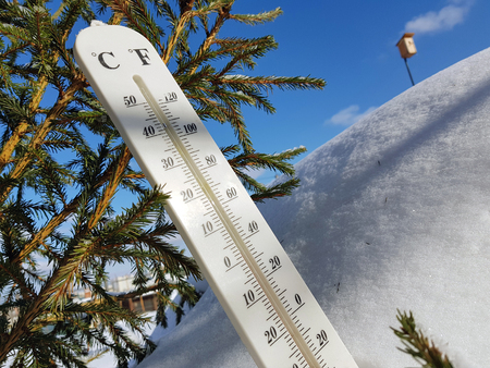 street thermometer with a temperature of Celsius and Fahrenheit on the snow next to a young spruce in winter or springの写真素材