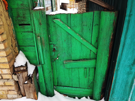 Very old gate with a fence at the entrance to a brick house on the background of snow in winterの写真素材
