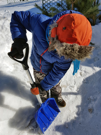 Snow shovel in the hands - a beautiful child cleans snow in the winter or spring in sunny weatherの写真素材