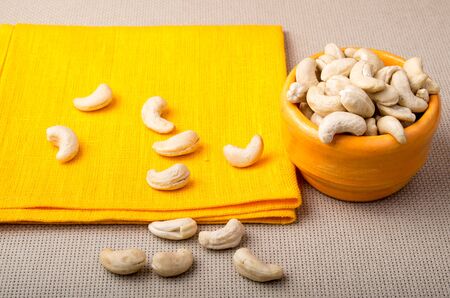 Selective focus on the tablecloth and raw cashew nuts in a small orange cup on orange napkin closeupの写真素材