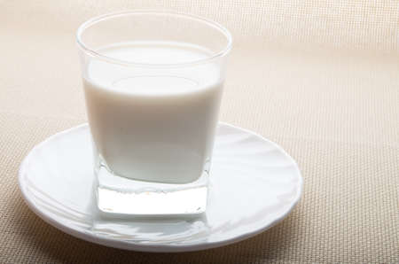One glass of milk on a white saucer backlight on textile backgroundの写真素材