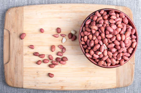 Top view of a brown bowl with raw peanuts on a wooden board on a background of gray tableclothの写真素材