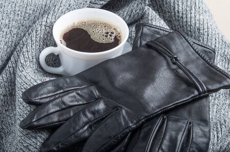 Grey wool scarf and leather gloves around the white cup of coffee with blur and shallow depth of focusの写真素材