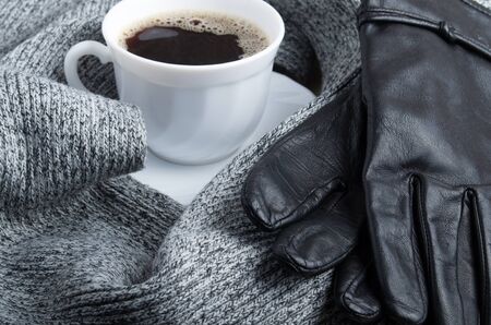 Grey wool scarf and leather gloves are surrounded by a hot cup of coffee with shallow depth of focusの写真素材