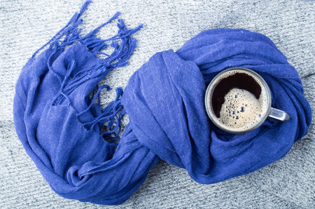Blue cotton scarf tied in a knot around the mug with hot coffee on a gray backgroundの写真素材