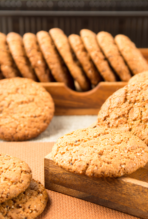 Group of oatmeal cookies on a wooden tray on a brown tablecloth with a very small depth of fieldの写真素材