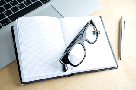 notebook, pen, glasses and laptop on the tableの写真素材
