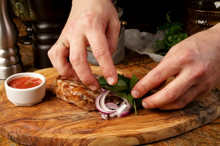 Closeup of chef's hands decorating meat steak with basil leaves.の写真素材