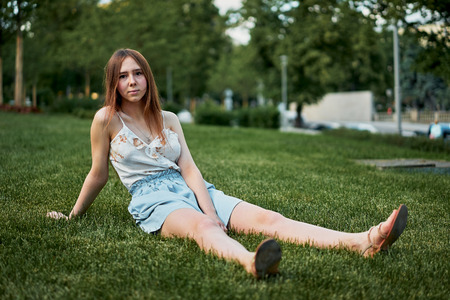 Pretty young girl sitting next to bike in grass and having a restの写真素材