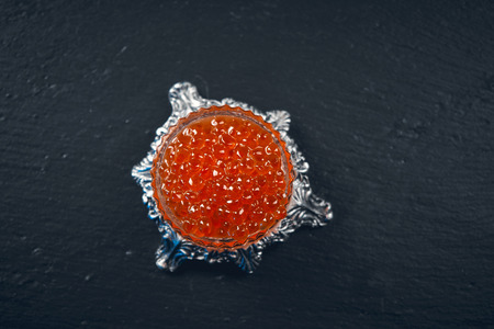 Red Caviar in a spoon. Caviar in bowl over black background. Close-up salmon caviar. Delicatessen. Gourmet food. Texture of caviar. Seafood.の写真素材