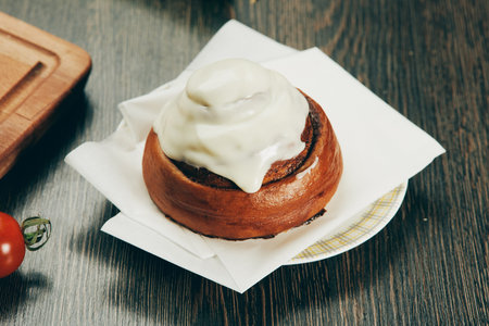 Sweet bun pastry with icing on a white plate on a wooden table