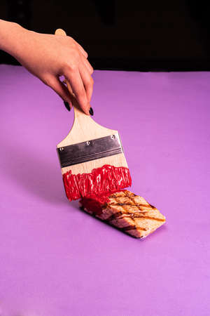 Paint fried meat with red paint with a brush on a lilac backgroundの写真素材