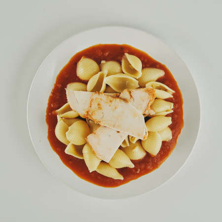 Pasta with tomato sauce and chicken breast pieces on a plateの写真素材