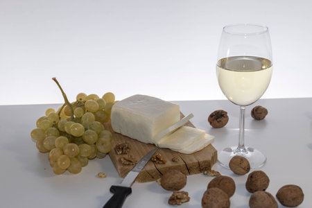 Chees, grapes, wallnuts and a glss of white wine on rustic wooden tableの写真素材