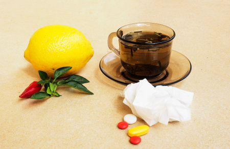 Hot tea for colds, pills and handkerchiefs on table,lemon and peppers, natural remedyの写真素材