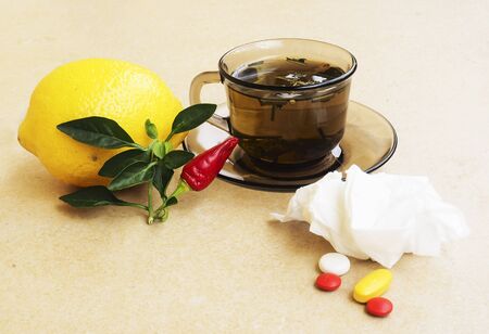 Hot tea for colds, pills and handkerchiefs on table,lemon and peppers, natural remedyの写真素材