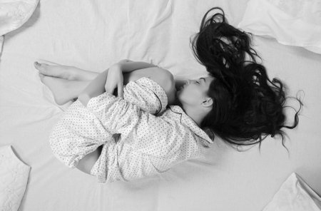 Girl sleeps in a white bed at home. Young woman sleeping in sleepwear on the white linen in bed at home, top view.の写真素材