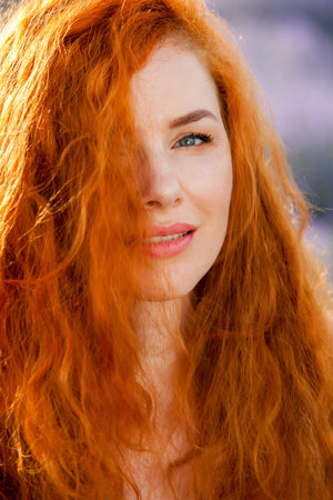 Summer portrait of a beautiful girl with long curly red hair. woman with long hair. European girl in...
