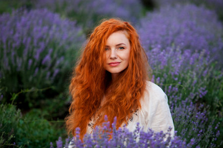 Summer portrait of a beautiful girl with long curly red hair. woman with long hair. European girl in lavander field. Wavy Red Hairの写真素材