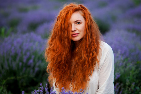 Summer portrait of a beautiful girl with long curly red hair. woman with long hair. European girl in lavander field. Wavy Red Hairの写真素材