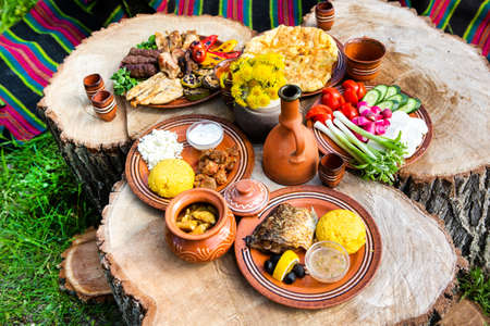 Homemade Romanian Food with grilled meat, polenta and vegetables Platter on camping. Romantic traditional Moldavian food outside on the wood table.の写真素材