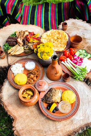 Homemade Romanian Food with grilled meat, polenta and vegetables Platter on camping. Romantic traditional Moldavian food outside on the wood table.の写真素材