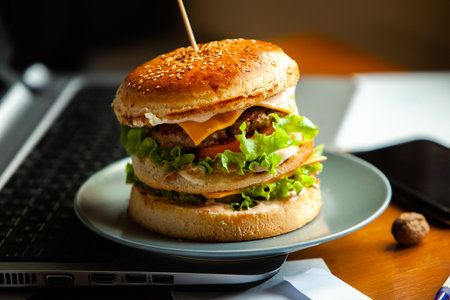 Cheeseburger on a plate with a laptop in the backgroundの写真素材