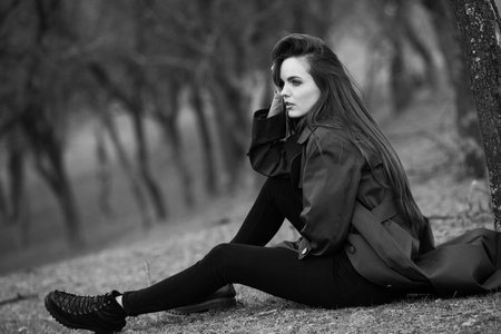 Beautiful young woman with long brown hair sitting on the ground in the parkの写真素材