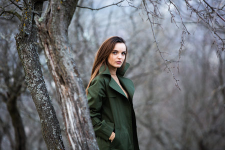 Portrait of a beautiful young brunette woman in green coat on the forest background