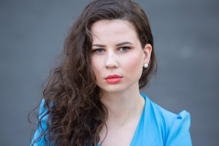 Portrait of a beautiful young brunette girl in a blue dress on a gray backgroundの写真素材