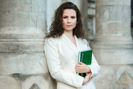 Portrait of a beautiful young brunette woman in white coat holding a bookの写真素材