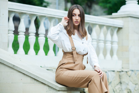 Portrait close up of young beautiful brunette woman in white blouse and brown pants, summer street outdoorsの写真素材
