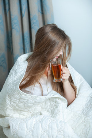 Sick young woman lying in bed and holding a cup of teaの写真素材