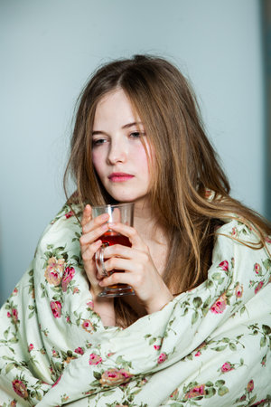 sick young woman in a blanket with a glass of hot drinkの写真素材